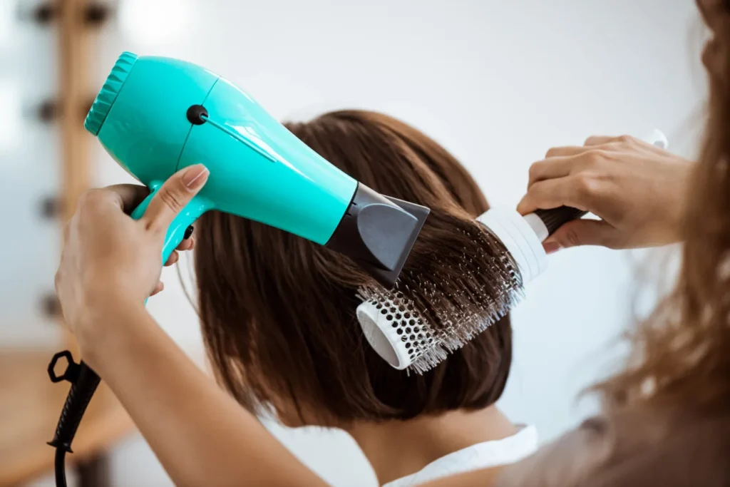 Hairdresser styling hair with blow dryer
